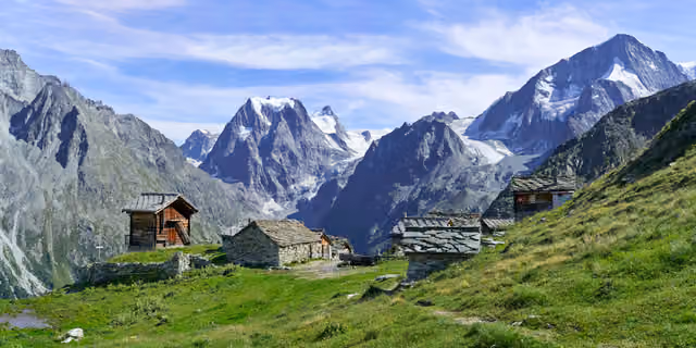 Stone and timber huts in an alpine pasture below snowy peaks